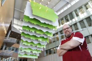 Jay Harmon stands in the atrium of the new buildings in front of its impressive artwork.