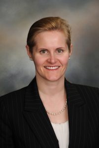 A smiling woman in a black suit jacket and white top