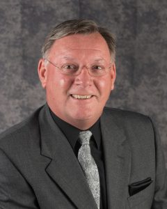 Headshot of Craig Denny on a gray background.