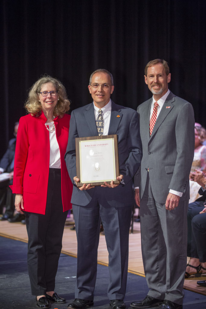 Ted Heindel holds a framed award alongside university leaders