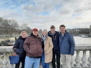 Former students poses with his parents, sister and brother in law. The family poses on a bridge over the Seine River in Paris, France