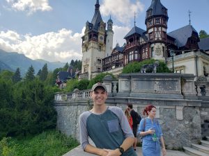 Former student poses with a castle, greenery and mountains in the back. Photo take in Romania