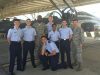 A group of ROTC cadets pose together. The cadets are wearing uniforms that include a light blue top and navy blue pants. The instructors are wearing camouflage. A jet is seen in the background of the shot.
