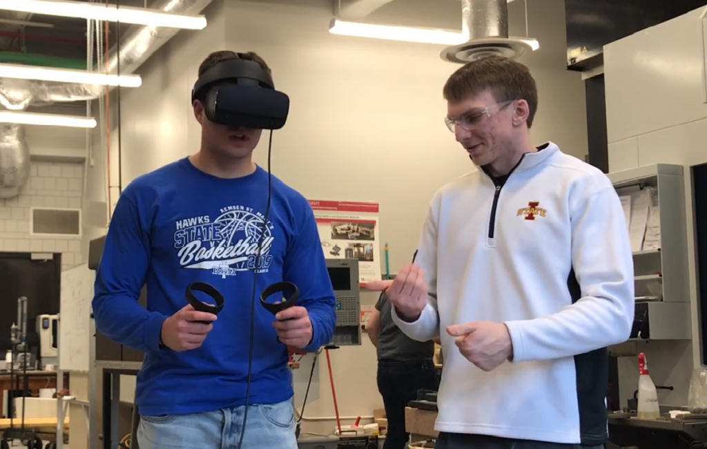 Student on left wears virtual reality goggles and simulates an environment, while the student on the right guides him. 