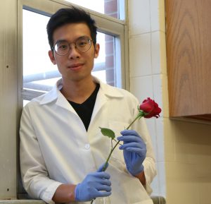 Photo of Andrew Martin in a lab coat and gloves, holding a red rose