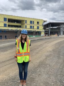 Student poses while wearing a hard hat and reflective vest on a construction work site.