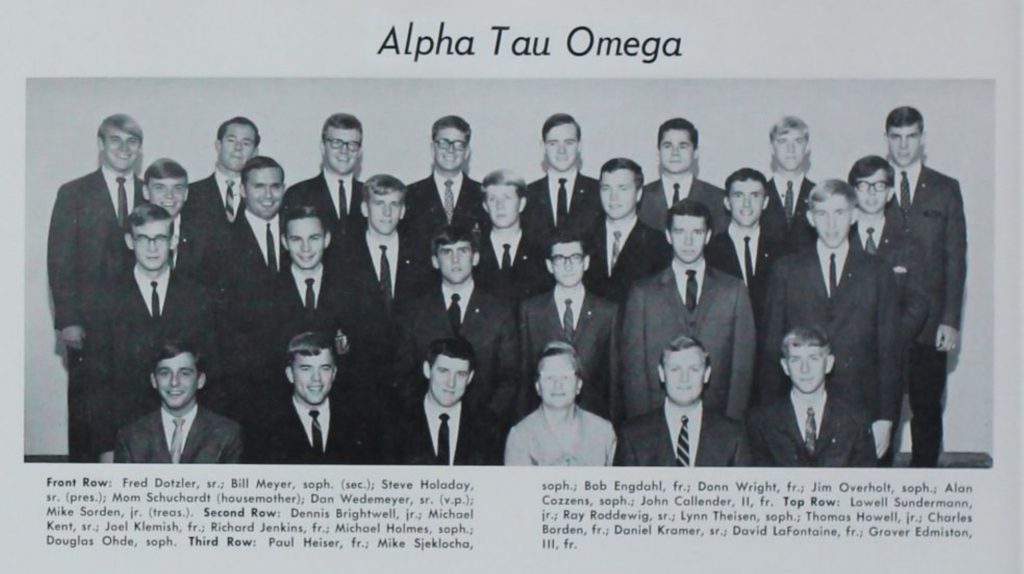 A black and white photo of brother from Alpha Tau Omega social fraternity. All of the brothers are wearing suits and ties, and most are smiling. The housemother - Mom Schuchardt - is the only female in the shot.