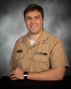 Ben McFarland poses in his military uniform. The uniform is tan and Ben wears several pins above his left breast pocket. 