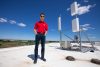 Hongwei Zhang standing on top of a building with blue sky behind him. There is hardware behind him for CyNet, an advanced wireless networking system that's a predecessor to the new ARA rural broadband project.