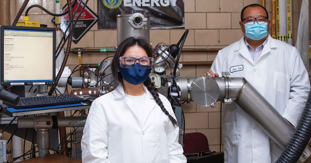 Two researchers stand in a lab near a melt-spinner instrument