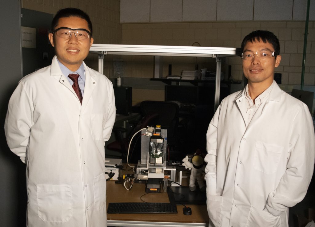 Materials science and engineering assistant professor Shan Jiang and industrial and manufacturing systems engineering assistant professor Hantang Qin pose inside a laboratory on the Iowa State University campus. A 3D printer can be seen in the background of the shot.