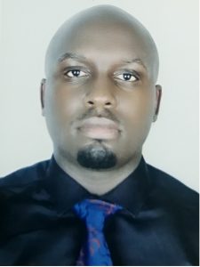 Headshot of Iowa State University alum Denis Bbosa. He is wearing a black shirt and a blue tie.