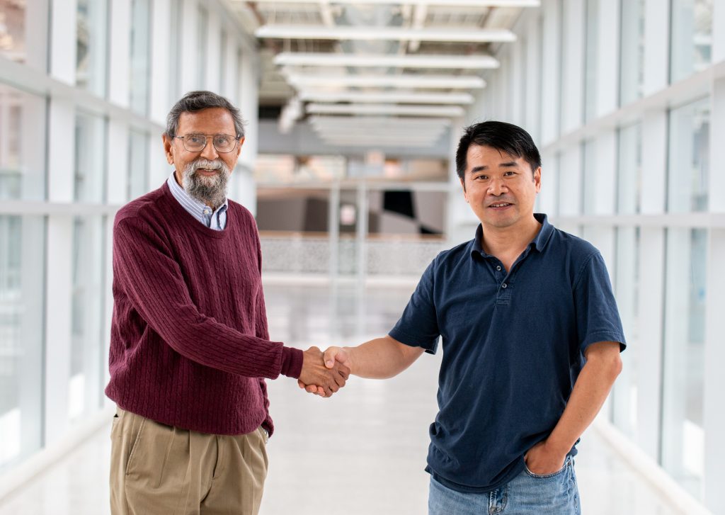 Vik Dalal and Liang Dong shake hands standing in a skywalk on campus.