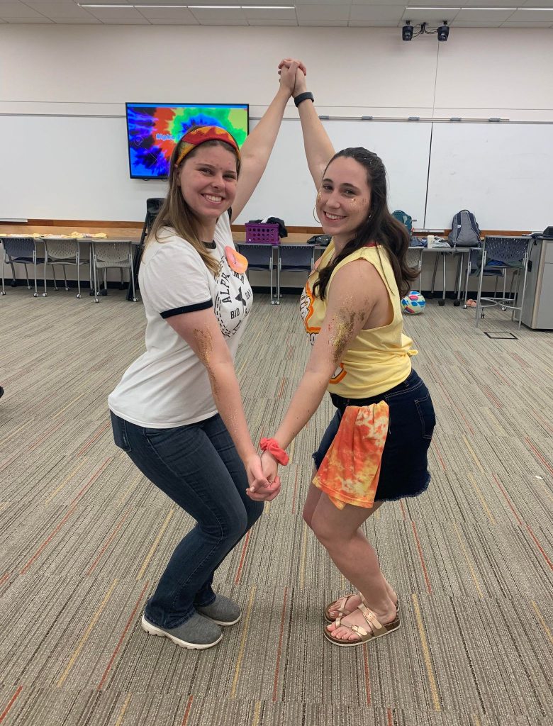 Two young ladies lock hands and pose together for a photo inside a building on the Iowa State University campus.