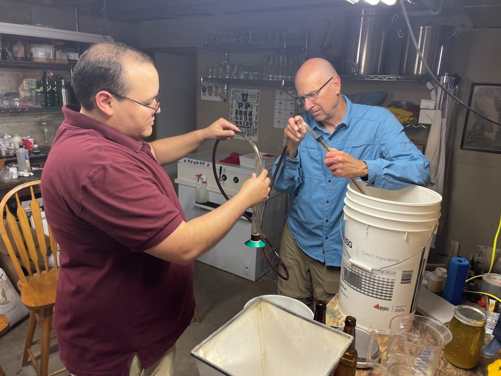 Two men hold up a tube as part of the beer brewing process.