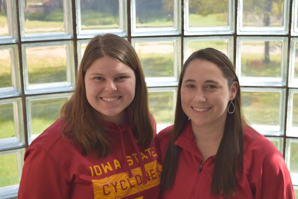 Two young ladies smile for the camera. They are both wearing red Iowa State University gear.