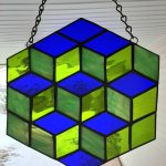 A strained glass panels that looks like 3D cubes stacked. The piece is green and blue.