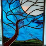 A stained-glass tree with a moon. This piece is mostly blue in color.