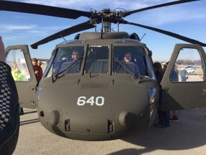 A graduate student and a professor sit inside a military helicopter and pose for a photo.