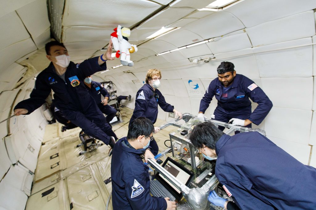 A shot of researchers inside an aircraft conducting research with a 3D printer. The researchers are "floating" as they are experiencing zero gravity.