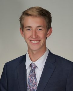 A photo of a college-aged man smiling and wearing a suit and tie. 