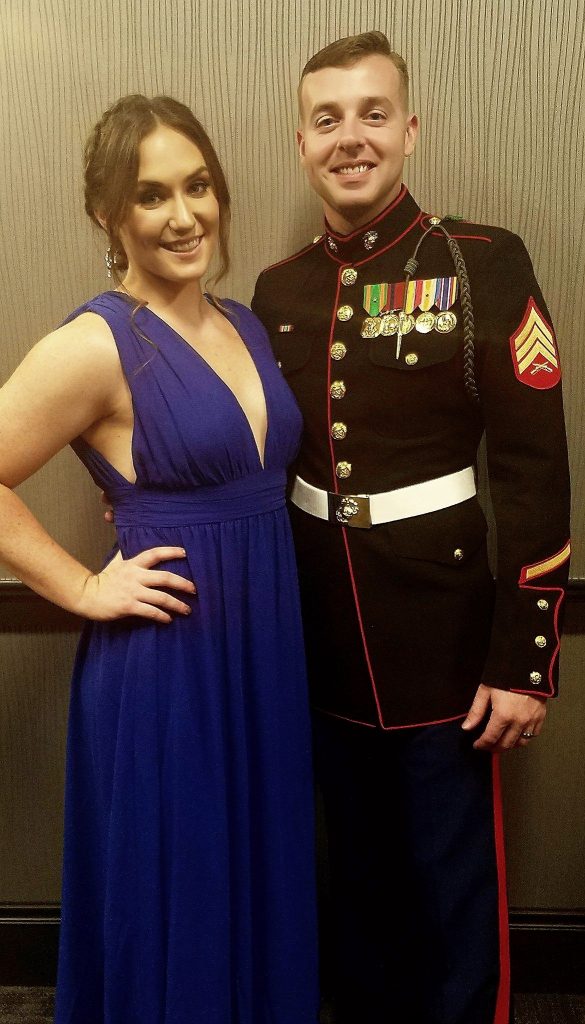 A couple pose together. The woman is wearing a blue dress, the man is wearing his Marines uniform.