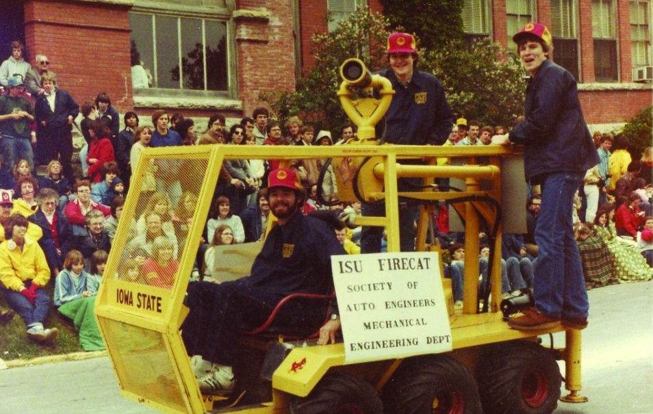 A photo from the 1970s or 80s. Three male students smile for the camera while riding the ISU FIRECAT, a vehicle designed by ISU engineering students to help firefighters.