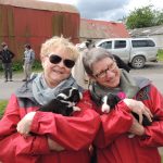 Two women pose while holding puppies