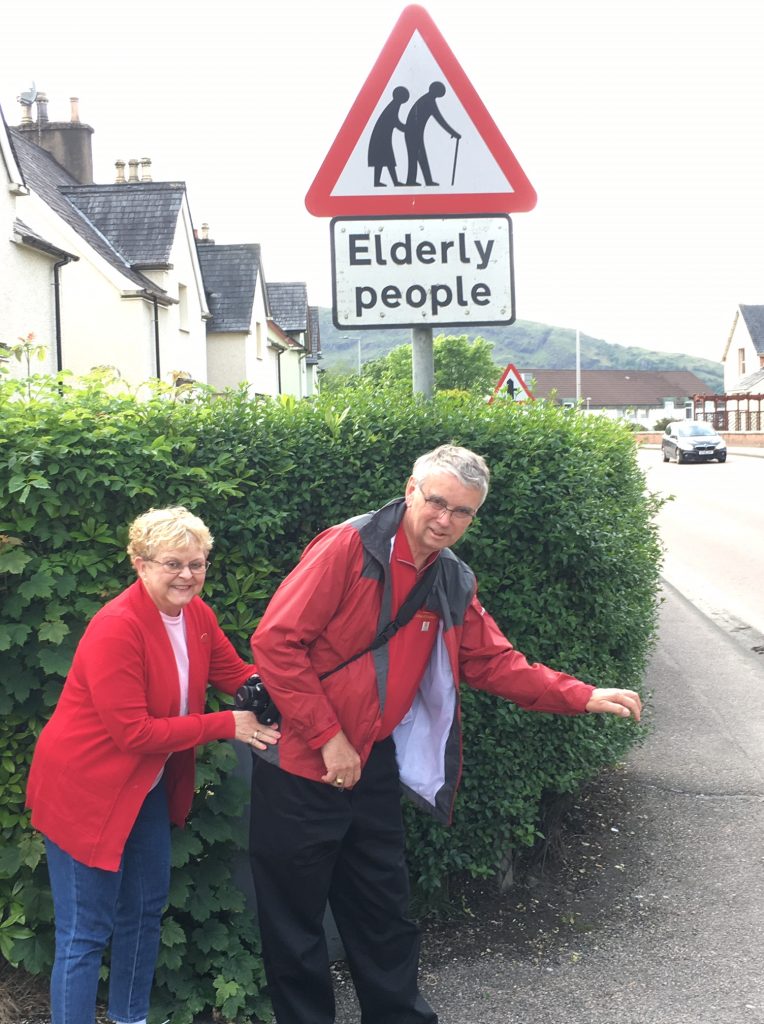 Pam and Larry attempt to mimic the pose of the two figures on an "Elderly people" sign