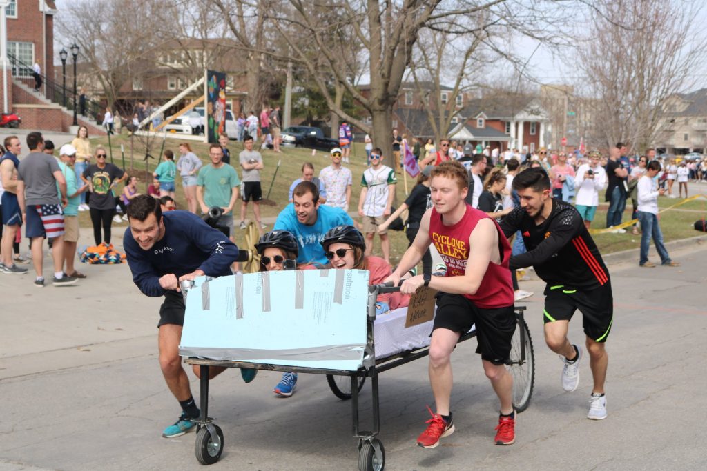 A group of college student push a bed frame with wheels welded to it as part of an Iowa State University tradition for Greek Week.
