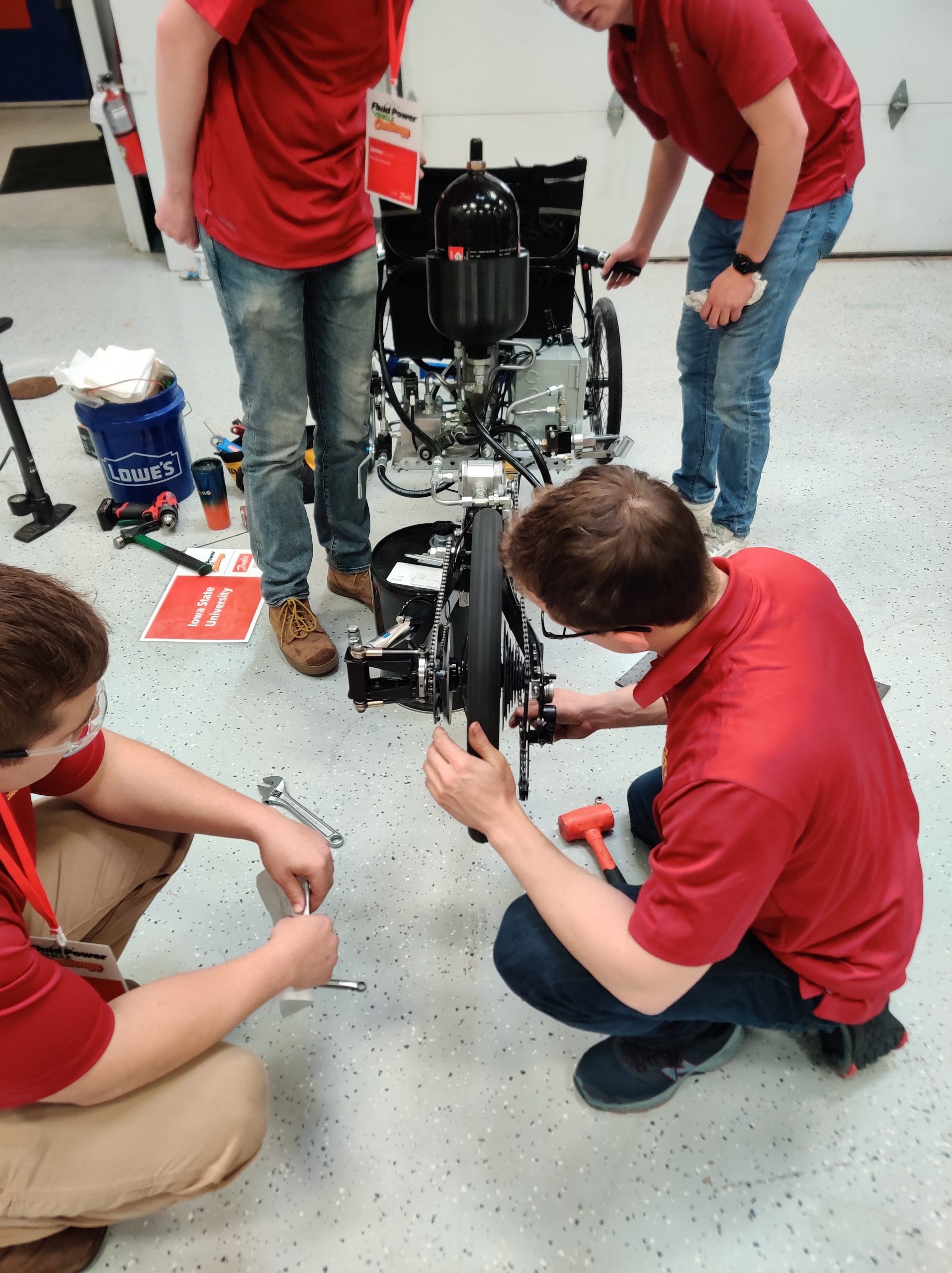 Photo of students on the ground working on the vehicle with tools