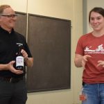 A student presents John with a bottle of beer