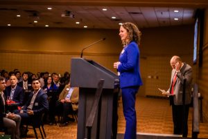 Photo of Beth speaking at the hall of fame/distinguished alumni banquet at a podium with industry partners in the audience