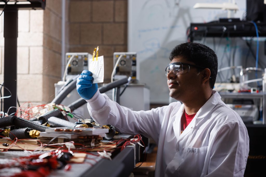 A student inside a lab holds up and examines a lithium-ion cell. 