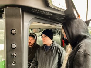 Three students sitting in the sprayer looking at the operation system