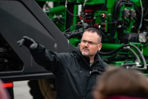 Professor Matt Darr standing in front of a sprayer pointing to the right