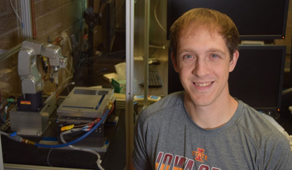 A young man poses next to a piece of machinery inside a mechanical engineering research lab.