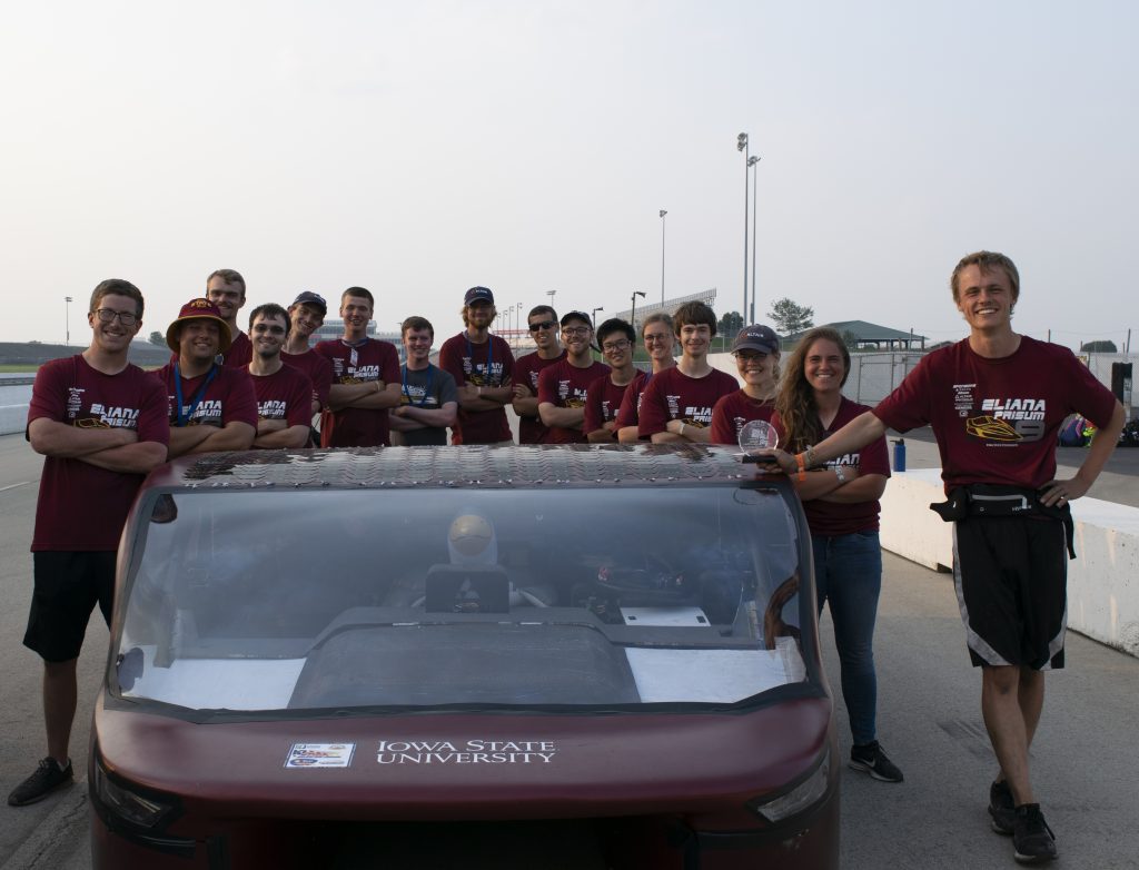 Students from the solar car team stand around their car and pose for the camera