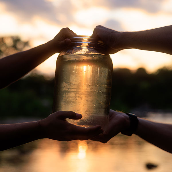 two sets of hands holding water sample in jar