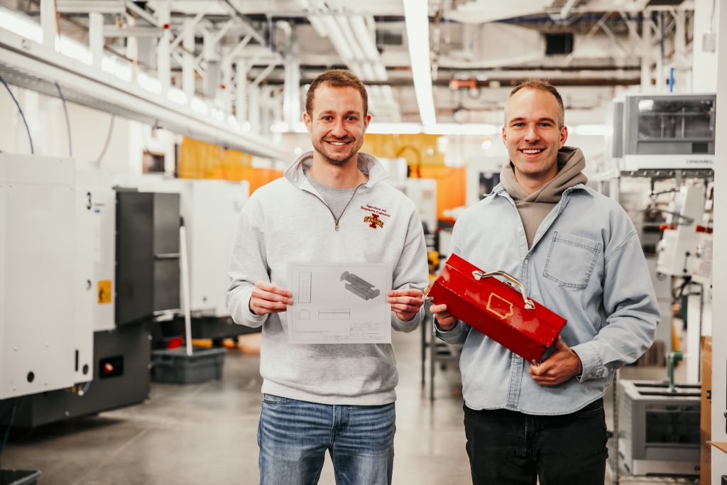 Photo of Bailey Adams holding a piece of paper with the designs on it, and Chad Dolphin holding a finished toolbox