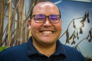 Worries behind him, Rodríguez-Ocasio smiles brightly in front of a mural of Iowa crops.