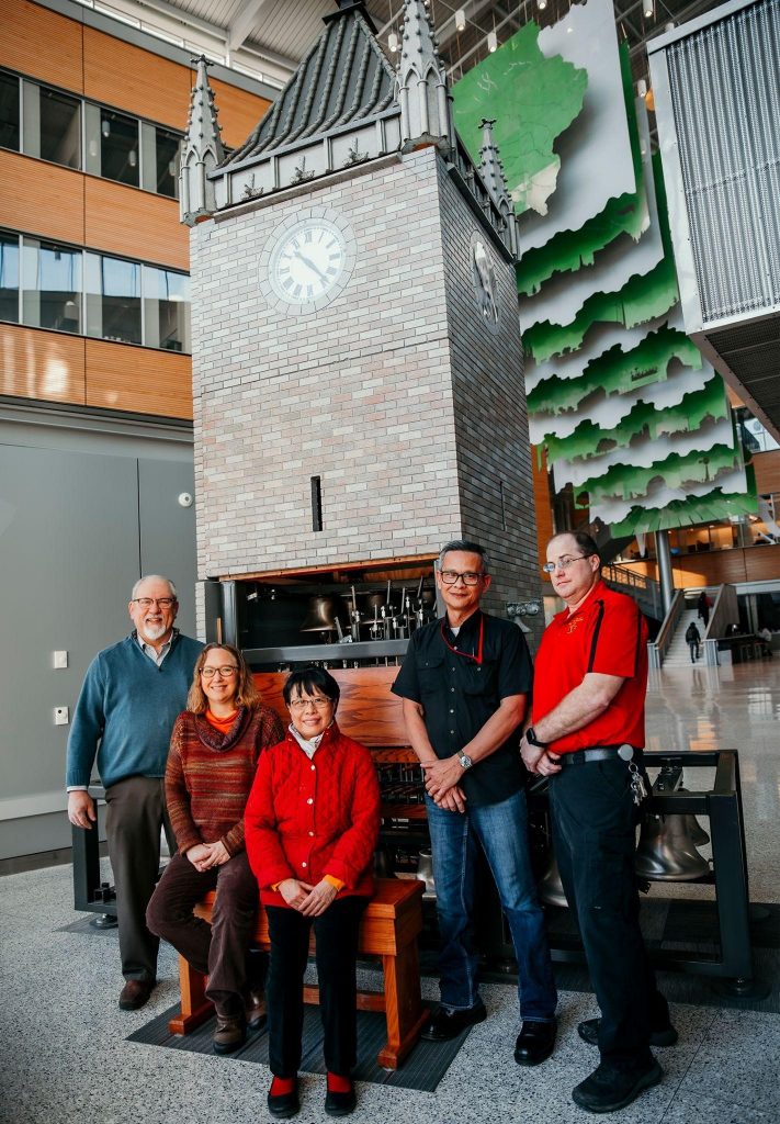 Vertical photo of team standing in front of the campanile model in the Sukup Atrium