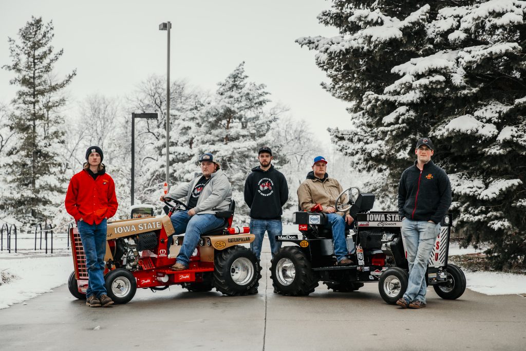 Five students sitting on and standing by tractors outside in the snow