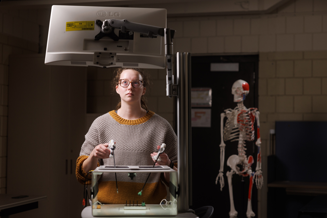 A student at a computer, a medical skeleton computer behind her