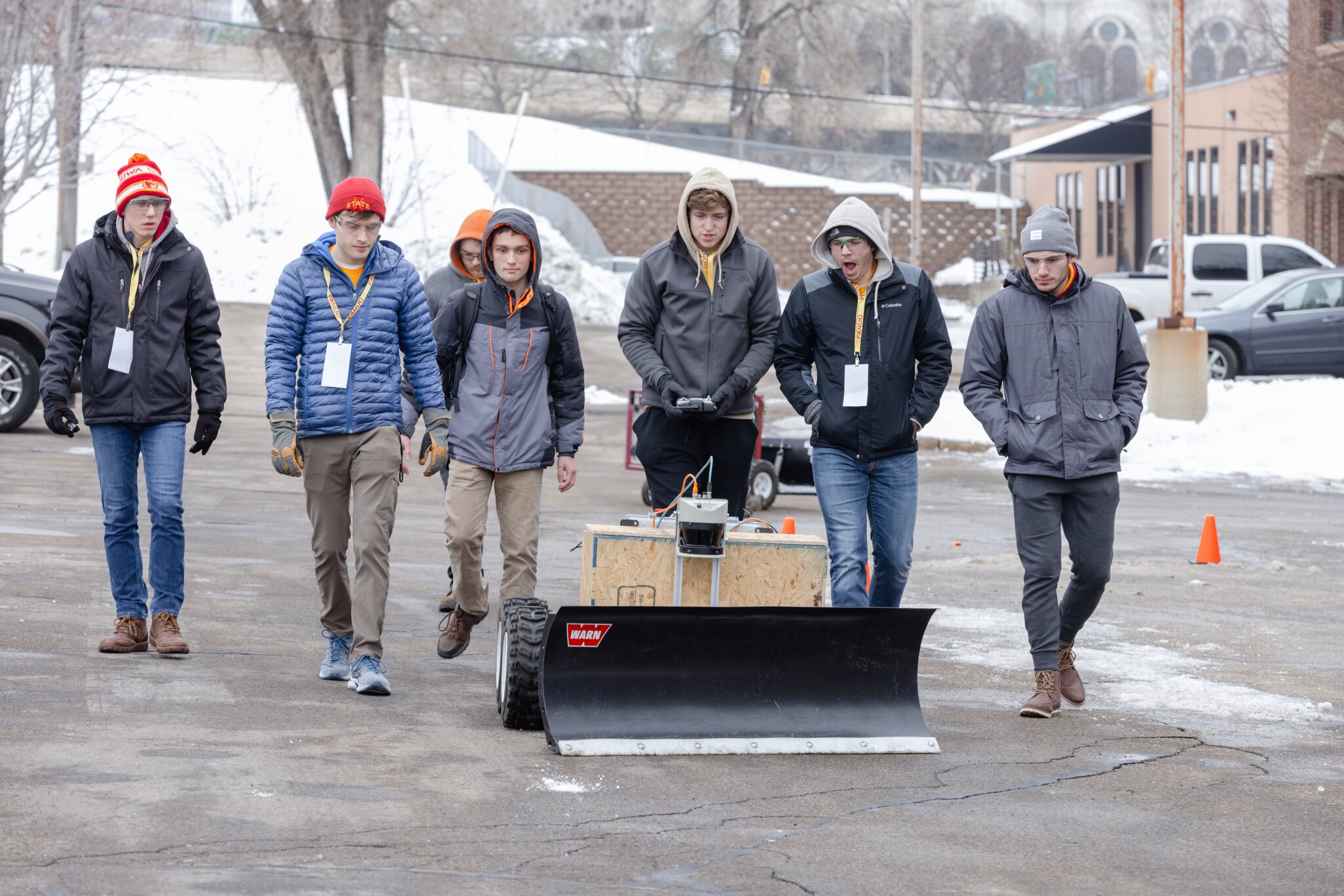 Students walk behind robotic snow plow pushing snow at contest.