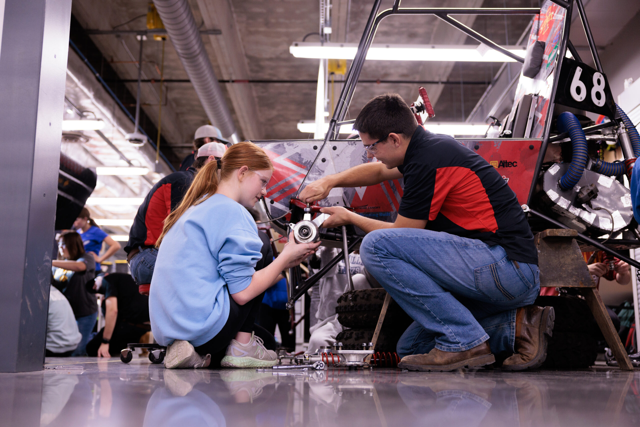 SAE student helps high schooler put together wheels to an ATV.