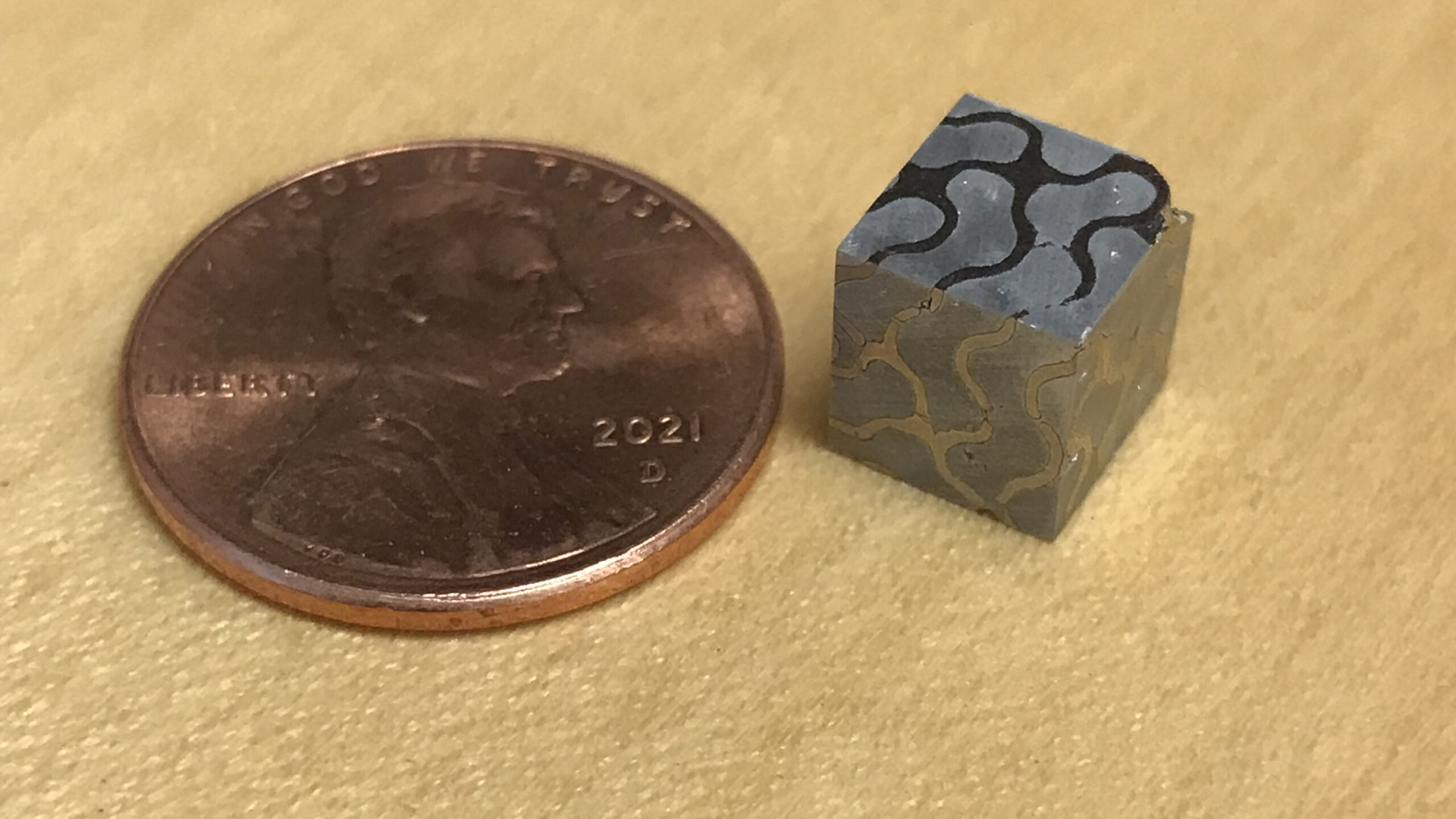 A cube of gradient metal next to a penny.