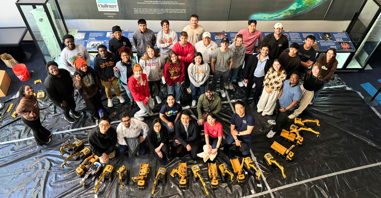 Student groups pose together in front of their remote controlled excavators. 