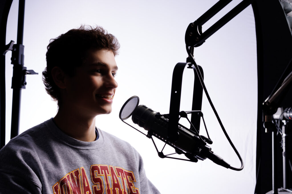 Male student speaking into a podcast mic on a white background.