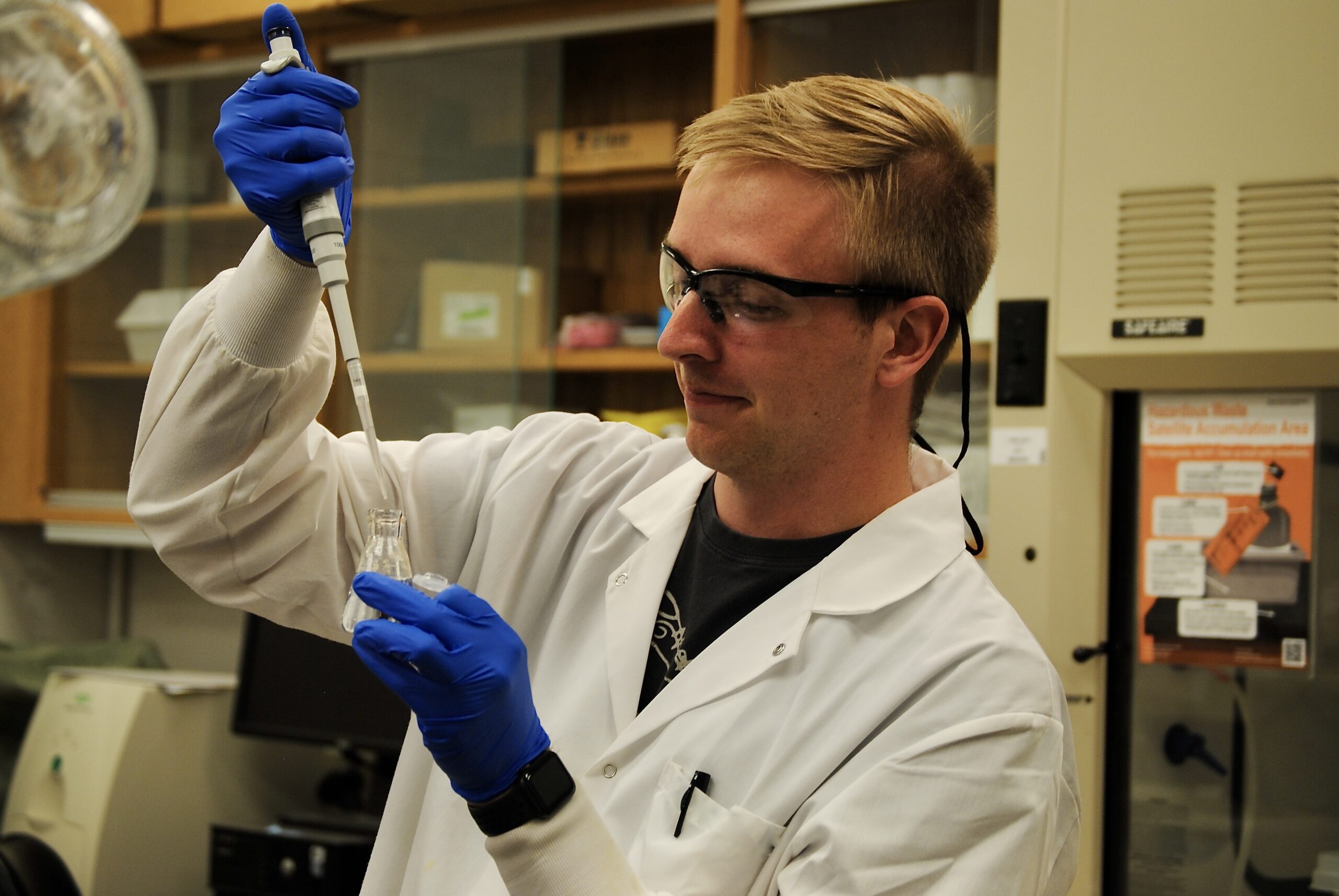Graduate student in lab coat taking sample of water.
